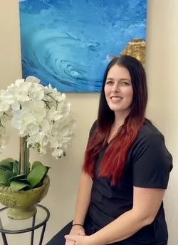 Hillary, Dental Hygienist, seated in black scrubs beside a white orchid at Tropical Smiles Dental